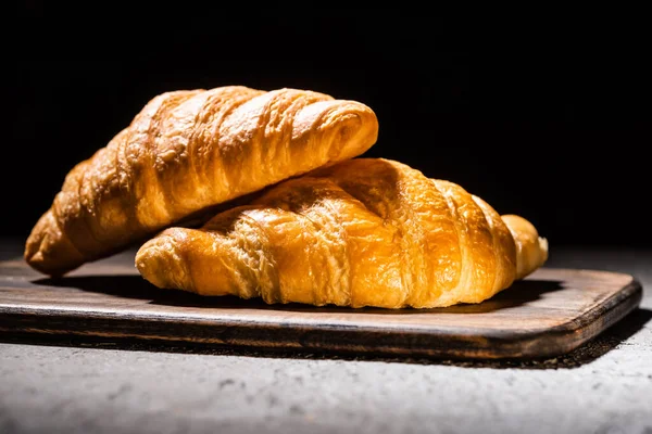 Croissants cozidos no forno fresco na placa de corte de madeira na superfície cinzenta concreta isolada no preto — Fotografia de Stock