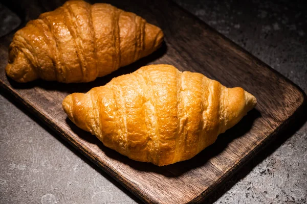Croissants cozidos no forno fresco na placa de corte de madeira na superfície cinzenta concreta no escuro — Fotografia de Stock