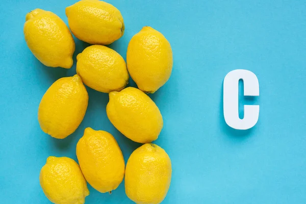 Top view of ripe yellow lemons and letter C on blue background — Stock Photo