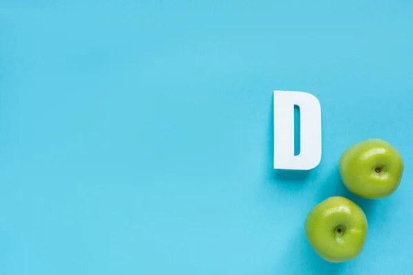 Top view of ripe green apples and letter D on blue background — Stock Photo