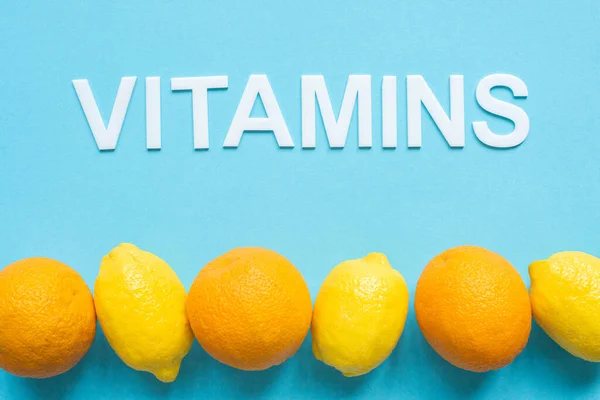 Ansicht von reifen gelben Zitronen, Orangen und Word-Vitaminen auf blauem Hintergrund — Stockfoto