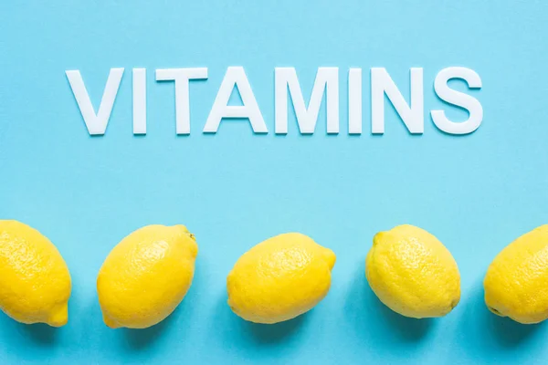 Vista superior de limones amarillos maduros y vitaminas palabra sobre fondo azul - foto de stock