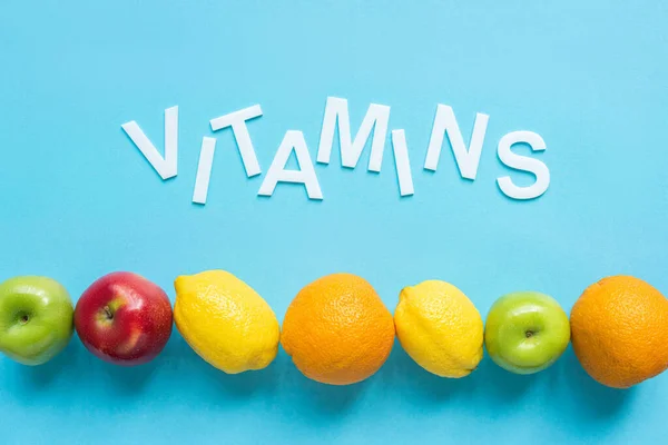 Top view of ripe fruits and word vitamins on blue background — Stock Photo