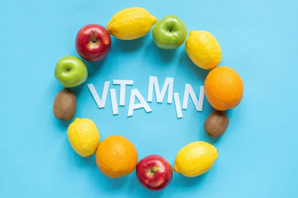 Vista superior de frutas maduras alrededor de la palabra vitamina sobre fondo azul - foto de stock