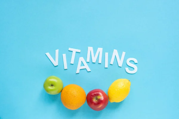 Vue du dessus des fruits mûrs et des vitamines de mot sur fond bleu — Photo de stock