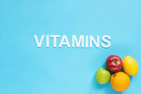 Vista superior de frutas maduras y vitaminas palabra sobre fondo azul - foto de stock