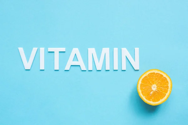 Верхний вид спелых оранжевый половина и слово витамин на голубом фоне — стоковое фото