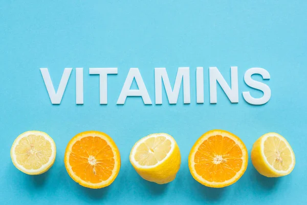 Верхний вид спелых апельсинов, половинки лимона и витамины слова на синем фоне — стоковое фото