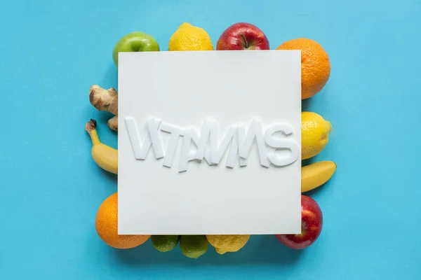 Top view of ripe fruits and word vitamins on white paper on blue background — Stock Photo