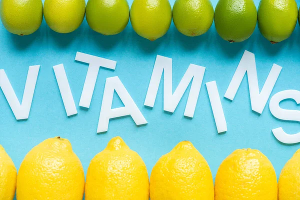 Вид зверху на стиглі жовті лимони і ліміти на синьому фоні зі словами вітаміни — стокове фото