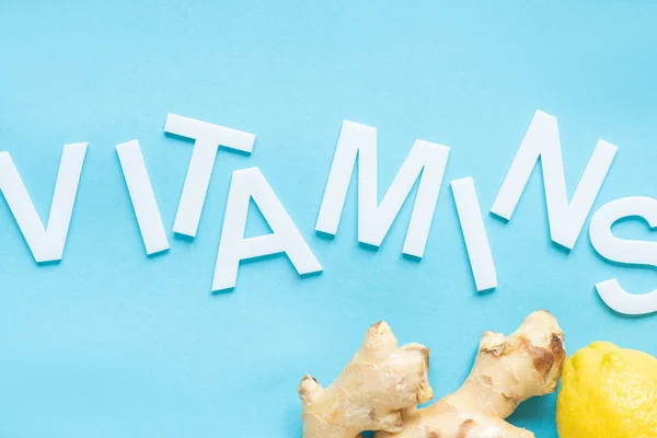 Vista dall'alto di limone giallo maturo e radice di zenzero su sfondo blu con vitamine parola — Foto stock
