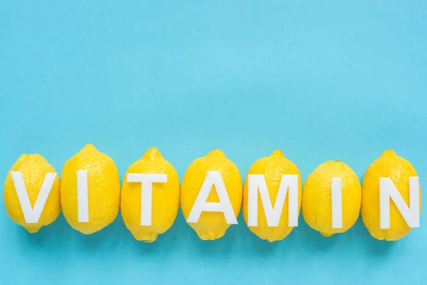Vista superior de limones amarillos maduros y palabra vitamina sobre fondo azul - foto de stock