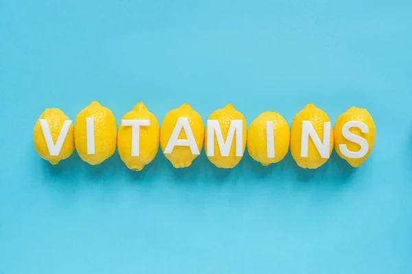 Top view of ripe yellow lemons and word vitamins on blue background — Stock Photo