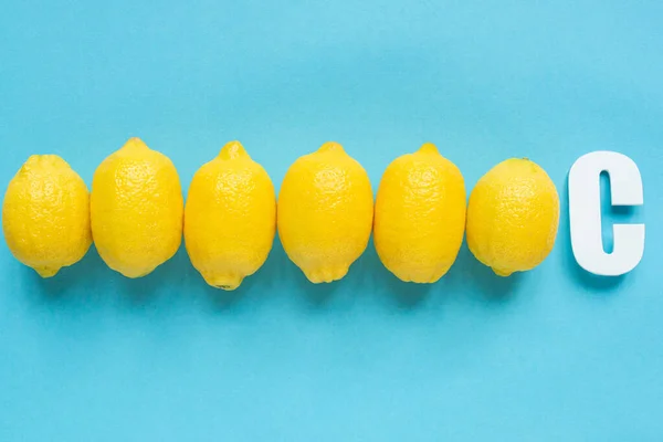 Vue du dessus des citrons jaunes mûrs et lettre C sur fond bleu — Photo de stock