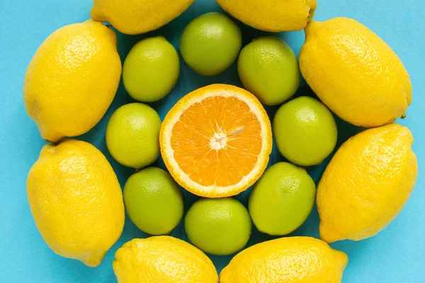 Vista superior de limones amarillos maduros, naranjas y limas dispuestas en círculos sobre fondo azul - foto de stock