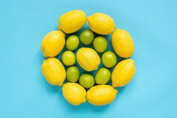 Vue du dessus des citrons jaunes mûrs et des citrons verts disposés en cercles sur fond bleu — Photo de stock