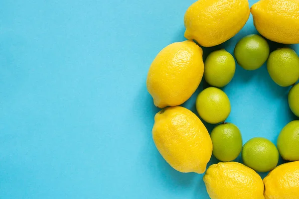 Vue du dessus des citrons jaunes mûrs et des citrons verts disposés en cercles sur fond bleu — Photo de stock