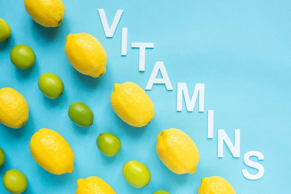 Flat lay with ripe yellow lemons, green limes and word vitamins on blue background — Stock Photo