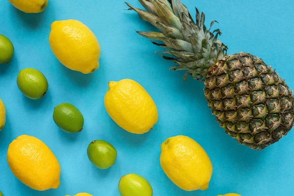 Plat avec des citrons jaunes mûrs, des citrons verts et de l'ananas sur fond bleu — Photo de stock