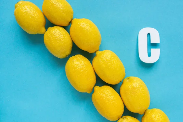 Tendido plano con limones amarillos maduros y letra C sobre fondo azul - foto de stock