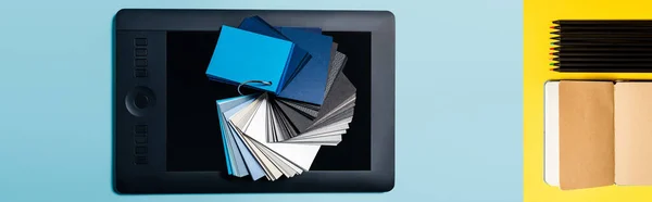 Collage of color samples on graphics tablet and notebook with pencils on blue and yellow background — Stock Photo