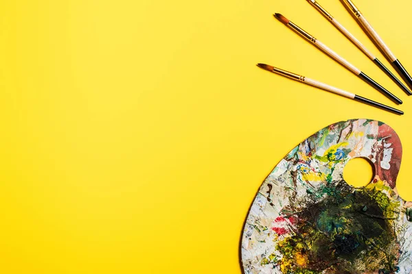 Vista superior de pinceles y paleta con pinceladas sobre superficie amarilla - foto de stock