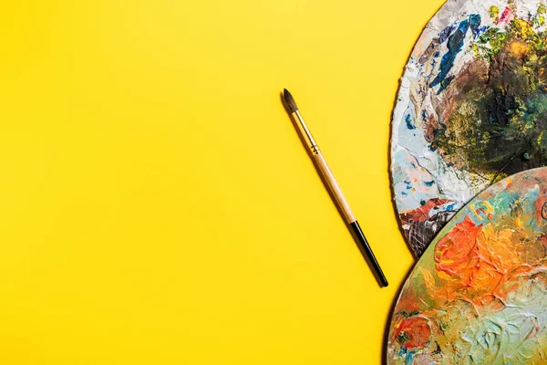 Top view of drawing brush and palettes on yellow surface — Stock Photo