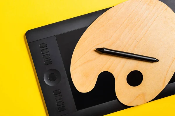 Vista superior da paleta de madeira e tablet gráfico com estilete na superfície amarela — Fotografia de Stock