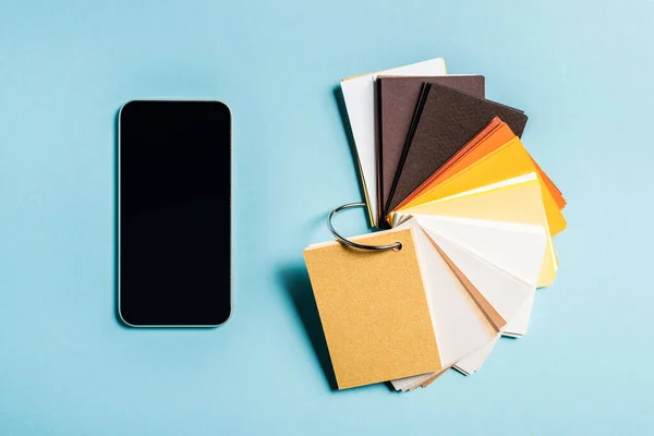 Vue du dessus des échantillons colorés et smartphone avec écran blanc sur fond bleu — Photo de stock