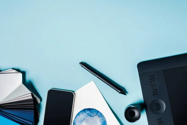 Vista superior del teléfono inteligente, muestras de color con gráficos tableta y acuarela dibujo sobre fondo azul - foto de stock