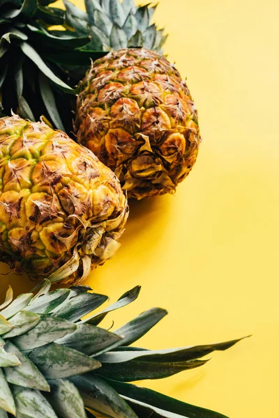 Selective focus of fresh ripe pineapples with green leaves on yellow background — Stock Photo