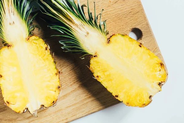 Vista dall'alto di succose metà ananas su tagliere in legno su sfondo bianco — Foto stock