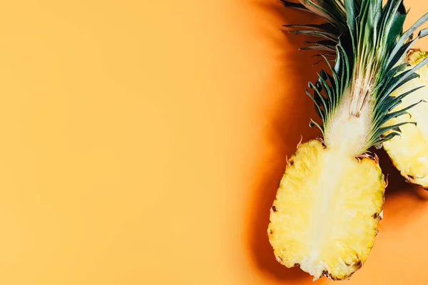 Top view of cut ripe pineapple with green leaves on orange background — Stock Photo