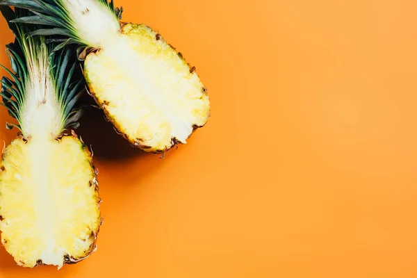 Draufsicht auf geschnittene reife Ananas mit grünen Blättern auf orangefarbenem Hintergrund — Stockfoto