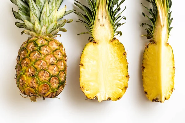 Plat avec des ananas coupés et entiers mûrs avec des feuilles vertes sur fond blanc — Photo de stock