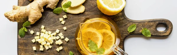 Top view of hot tea near ginger root, lemon and mint on wooden cutting board on white background, panoramic shot — Stock Photo