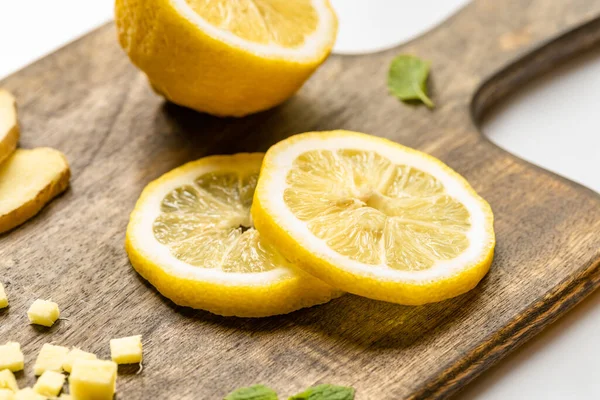 Vista da vicino di radice di zenzero tritata, limone e menta tagliati a fette su tagliere in legno su sfondo bianco — Foto stock