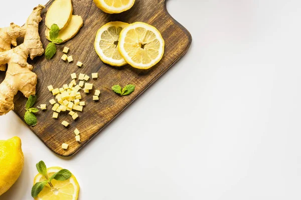 Vue du dessus de racine de gingembre, citron et menthe sur planche à découper en bois sur fond blanc — Photo de stock