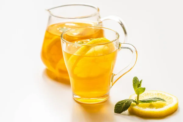 Foyer sélectif de thé chaud dans le verre et théière près de citron et menthe sur fond blanc — Photo de stock