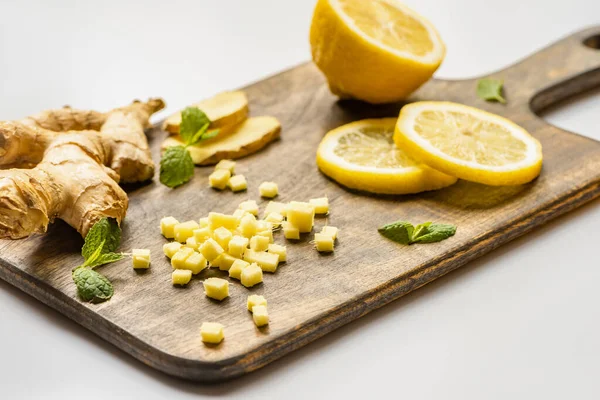 Foco seletivo de raiz de gengibre, limão e hortelã na placa de corte de madeira no fundo branco — Fotografia de Stock