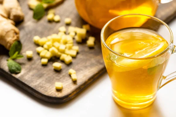 Messa a fuoco selettiva del tè caldo vicino alla radice di zenzero, limone e menta sul tagliere in legno su sfondo bianco — Foto stock