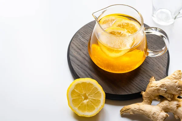 Thé chaud en théière sur planche de bois près de la racine de gingembre, citron sur fond blanc — Photo de stock