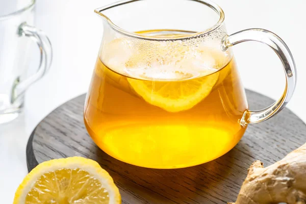 Vue rapprochée du thé chaud en théière sur planche de bois près de la racine de gingembre, citron sur fond blanc — Photo de stock