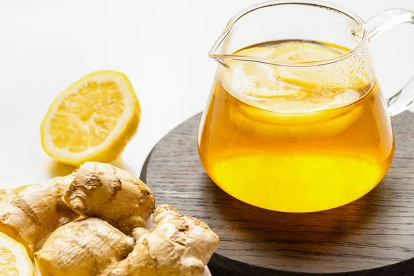 Горячий чай в чайнике на деревянной доске возле корня имбиря, лимон на белом фоне — стоковое фото