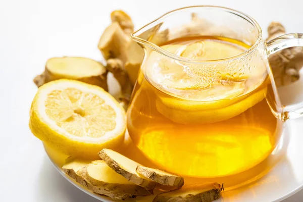 Thé chaud dans la théière près de la racine de gingembre, citron sur plaque sur fond blanc — Photo de stock