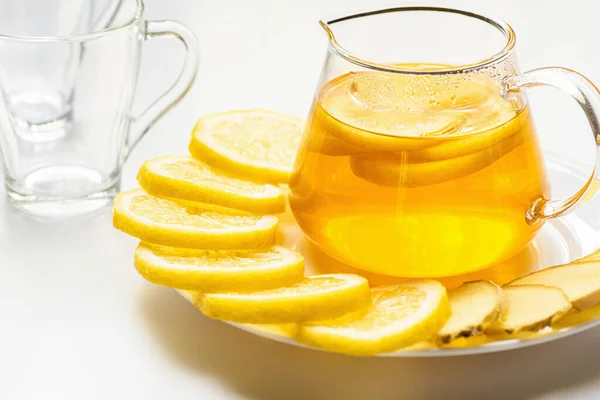 Hot tea in glass teapot with lemon slices and ginger on white background — Stock Photo
