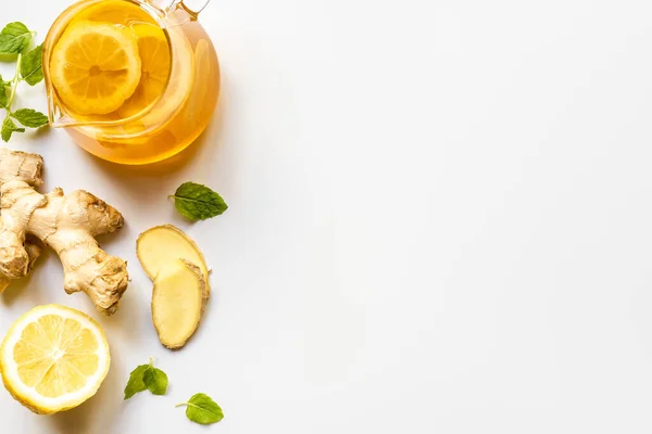 Vue du dessus du thé chaud dans une théière en verre près de la racine de gingembre, citron et menthe sur fond blanc — Photo de stock