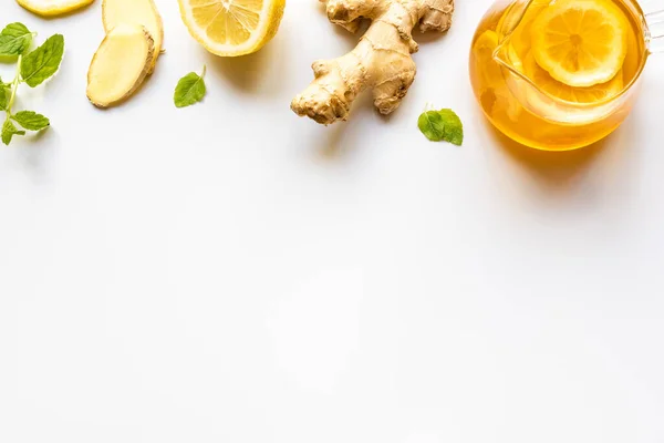 Vue du dessus du thé chaud dans une théière en verre près de la racine de gingembre, citron et menthe sur fond blanc — Photo de stock