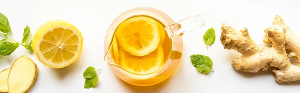 Top view of hot tea in glass teapot near ginger root, lemon and mint on white background, panoramic shot — Stock Photo