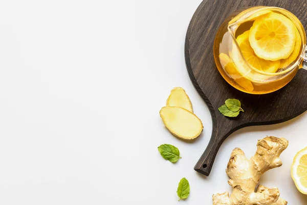 Vue du dessus du thé chaud en théière servi sur une planche de bois près de la racine de gingembre, citron et menthe sur fond blanc — Photo de stock